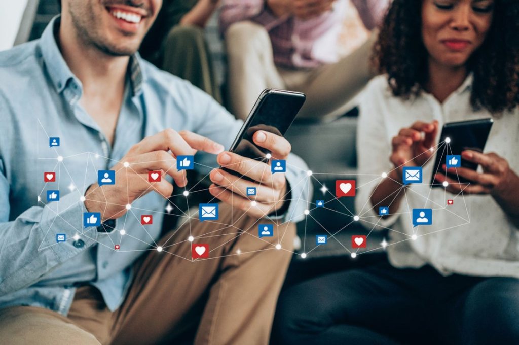 Duas pessoas navegando em seus smartphones, conectadas por uma rede de ícones de mídia social.
