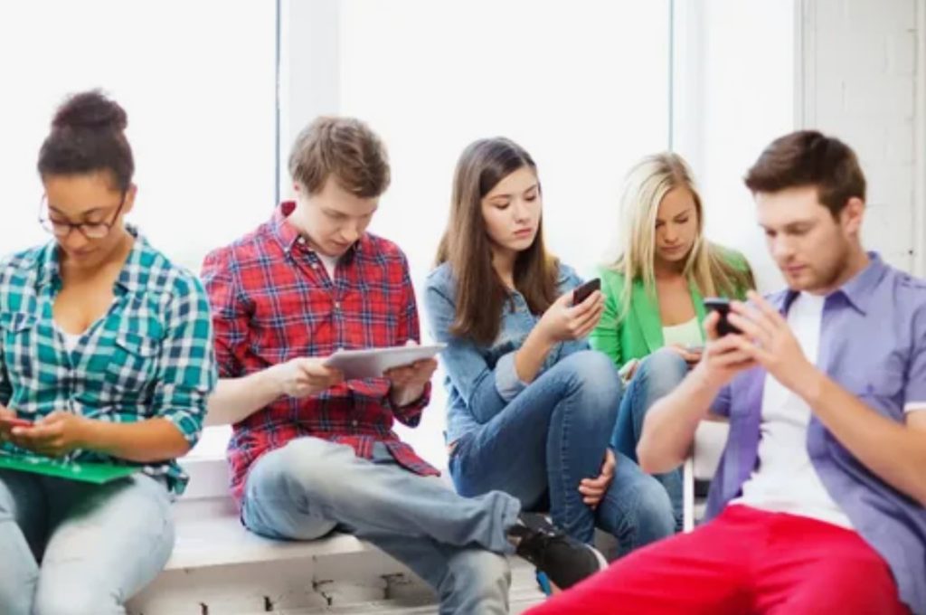 Jovens em uma sala de aula usando dispositivos móveis.