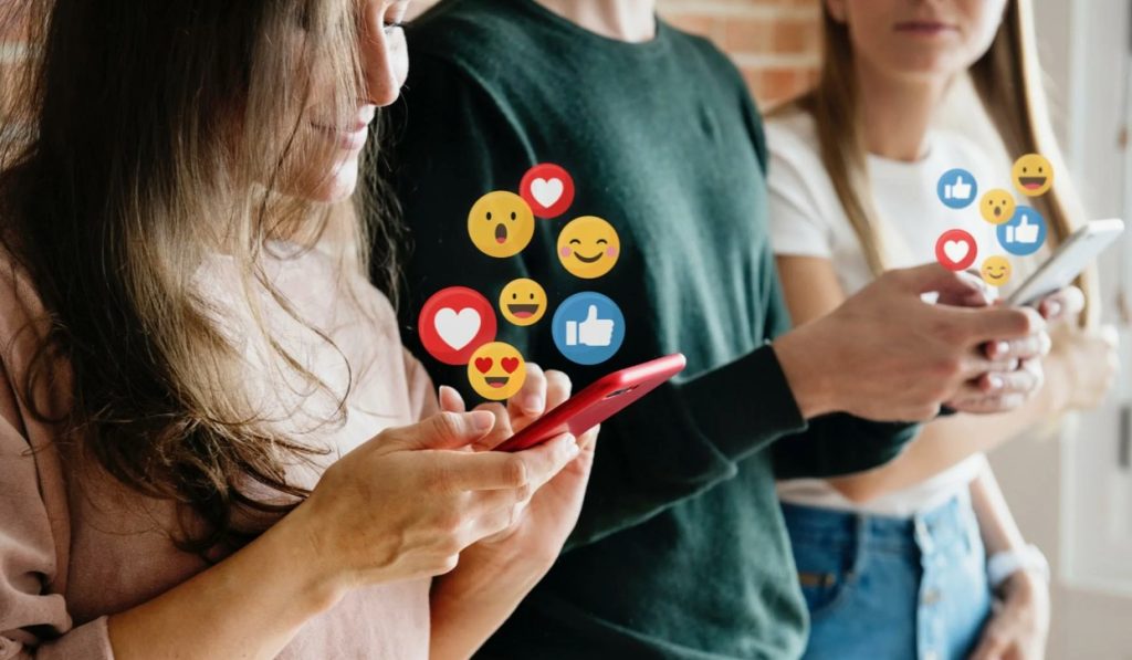 Três amigos usando smartphones com emoticons e curtidas virtuais.