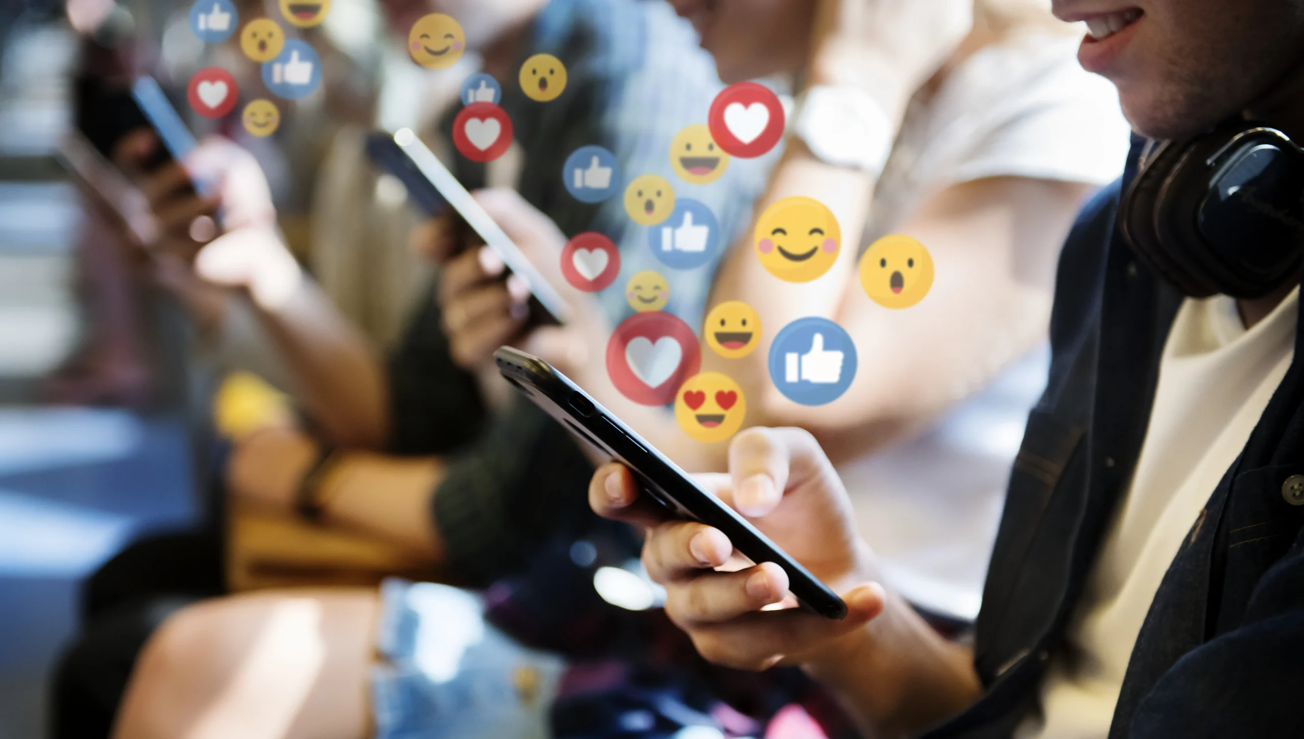 Mãos segurando um smartphone com notificações de curtidas e emoticons.