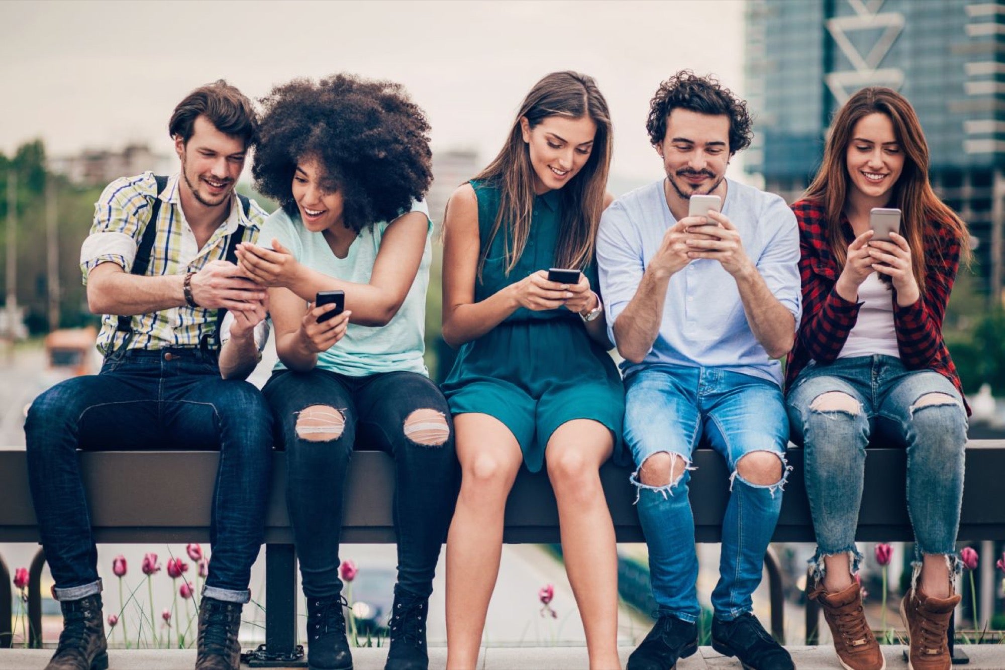 Grupo de amigos sentados lado a lado usando seus smartphones.
