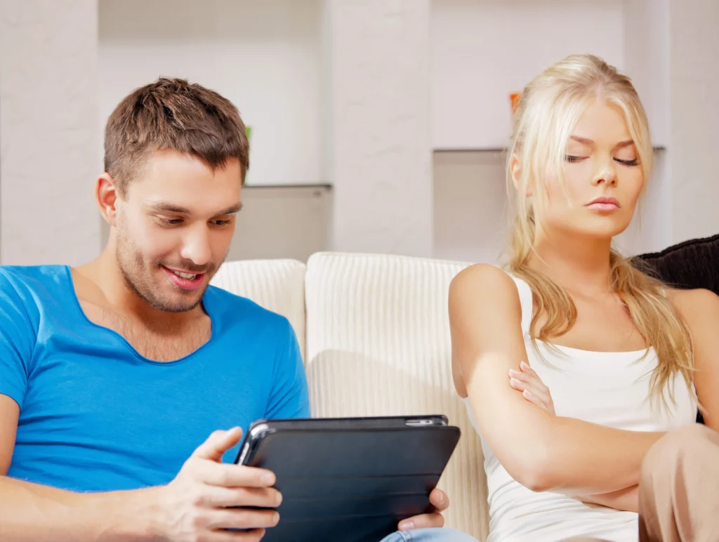 Um casal sentado em um sofá, um olhando para um tablet enquanto o outro parece desapontado.