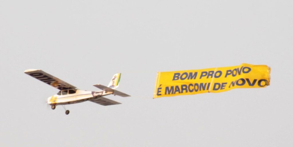 Avião rebocando faixa com mensagem política no céu.