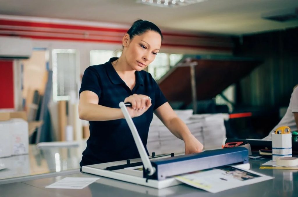 Funcionária da gráfica utilizando uma guilhotina para cortar impressos.