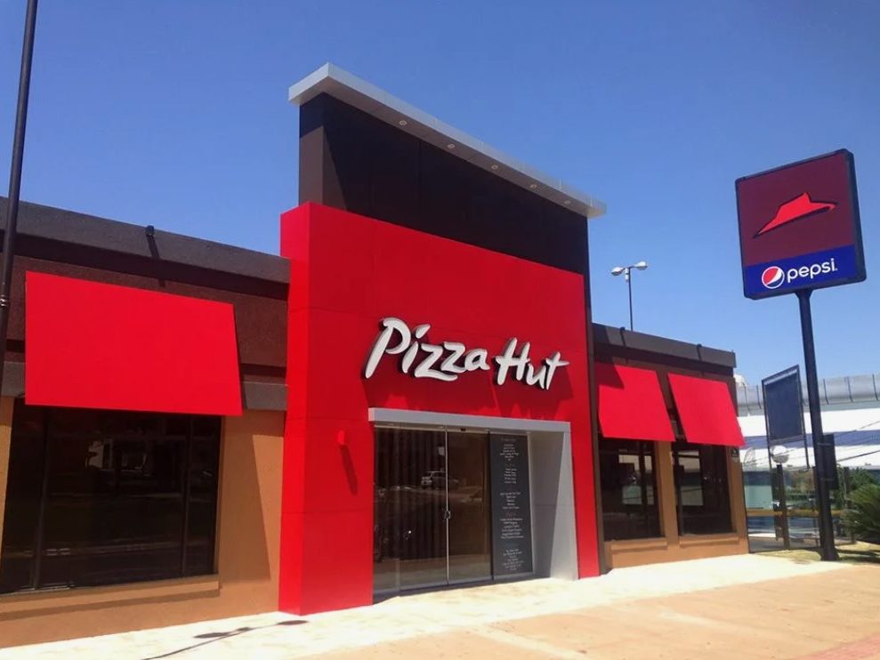 Fachada de um restaurante Pizza Hut com logotipo branco em uma fachada vermelha.