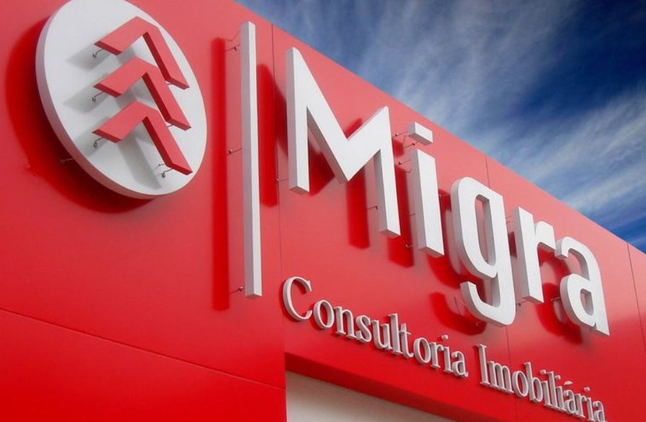 Fachada da Migra Consultoria Imobiliária com letreiro branco em fundo vermelho.