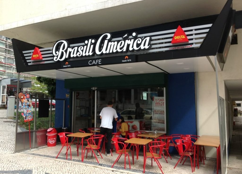 Fachada de café com design moderno, cadeiras e mesas vermelhas.