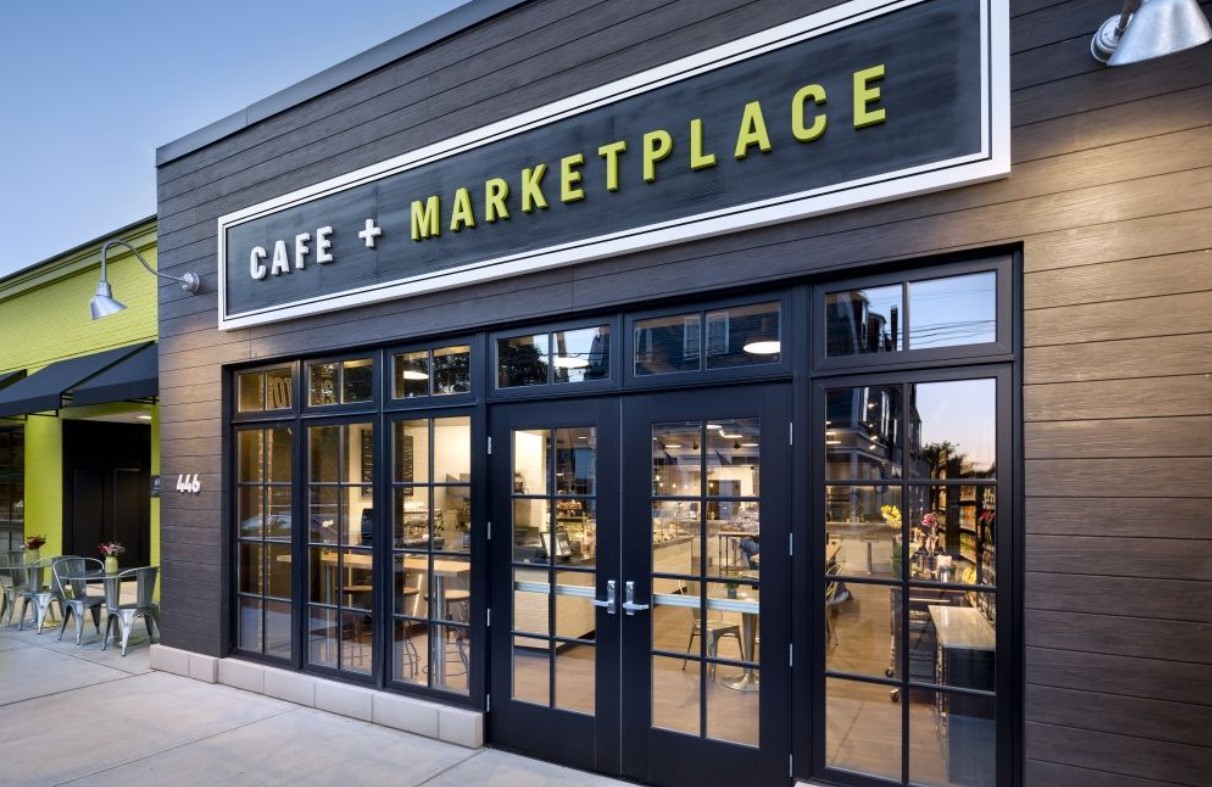 Fachada do Cafe + Marketplace com janelas grandes e design moderno.
