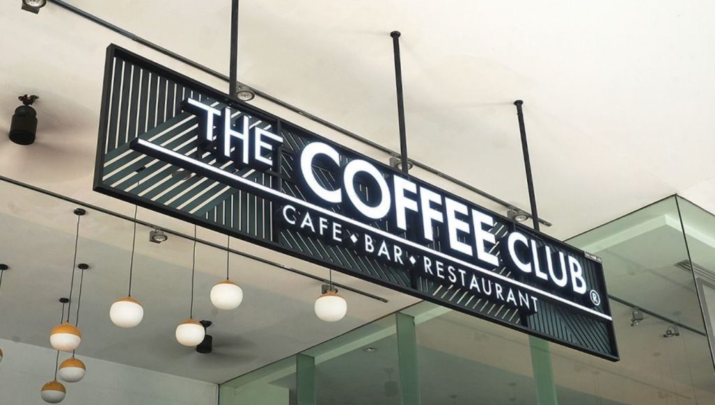 Letreiro da cafeteria The Coffee Club com design moderno e iluminação.