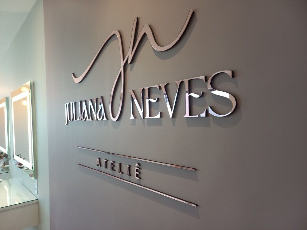 Letreiro \"Juliana Neves Ateliê\" em letras metálicas grandes em uma parede neutra.