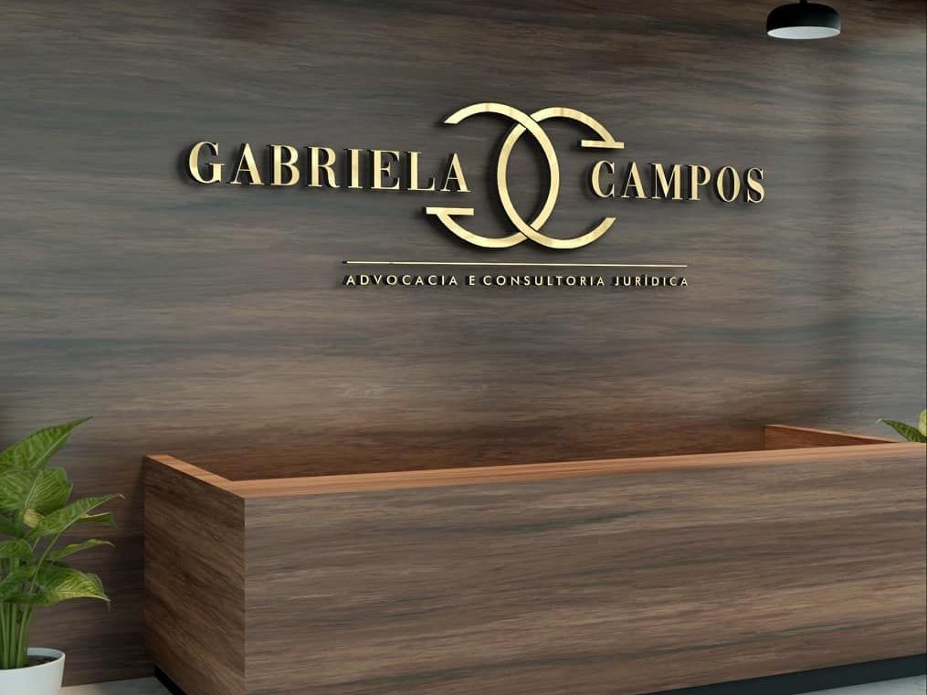 Área de recepção de um escritório com balcão de madeira e parede com logo dourado \"GABRIELA CAMPOS\".