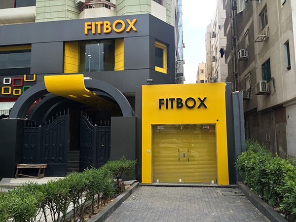 Fachada da FITBOX com design moderno em cinza e amarelo.