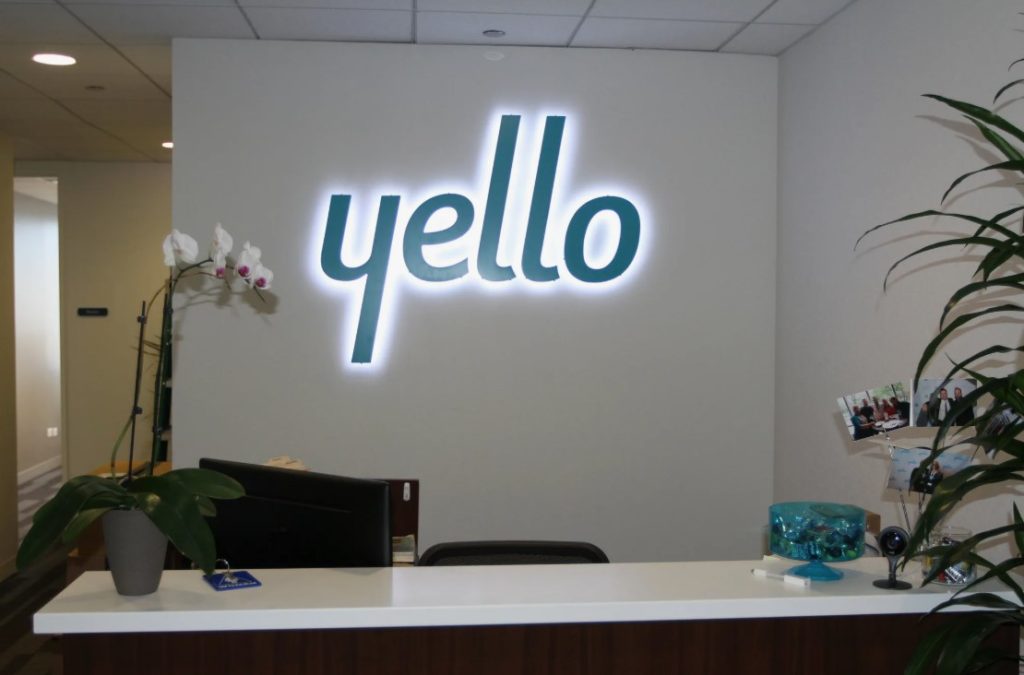 Recepção moderna com letreiro iluminado "yello" na parede.
