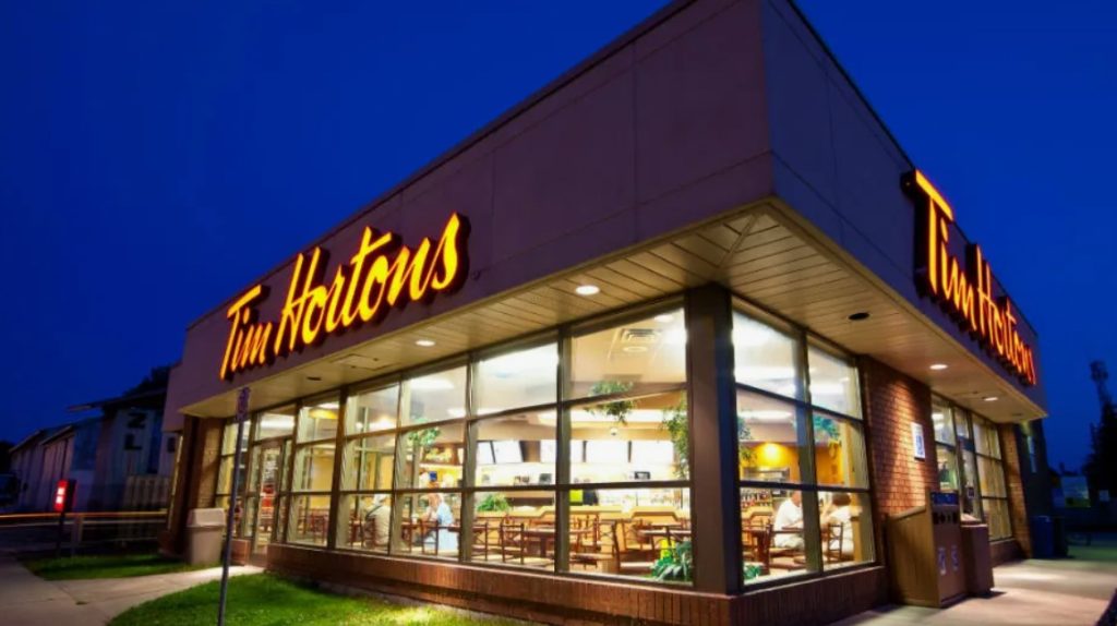 Fachada iluminada do Tim Hortons à noite, com grandes janelas e o logotipo iluminado.