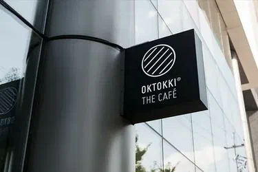 Fachada do OKTOKKI THE CAFÉ com letreiro branco em fundo preto e design moderno.