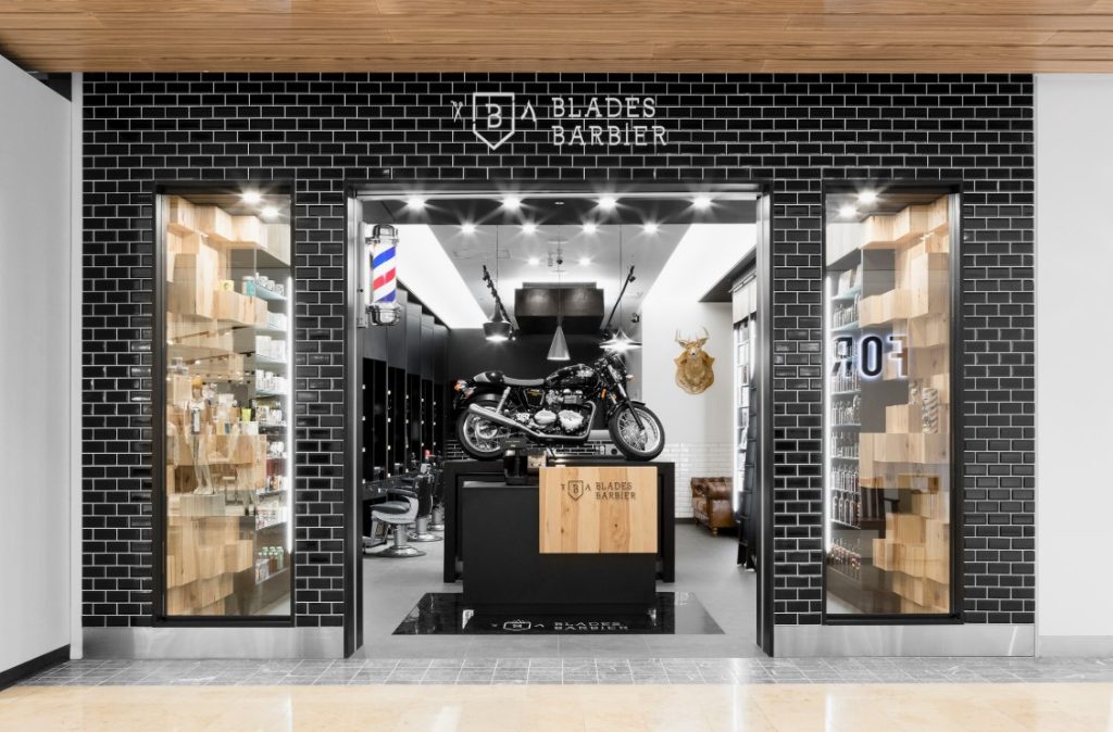 Fachada moderna da Blades Barbier com tijolos pretos e vitrine ampla.
