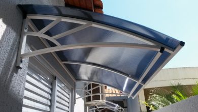 Toldo curvo de policarbonato sobre janela com estrutura metálica branca.