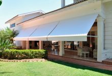 Casa moderna branca com elegantes toldos retráteis no pátio ensolarado.