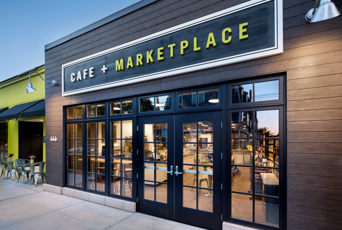 Fachada moderna do CAFE + MARKETPLACE com janelas de vidro amplas.