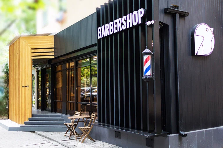 Barbearia com fachada preta, janelas de vidro e poleiro de barbearia clássico.