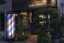 Fachada moderna de barbearia com placa preta e letras brancas.