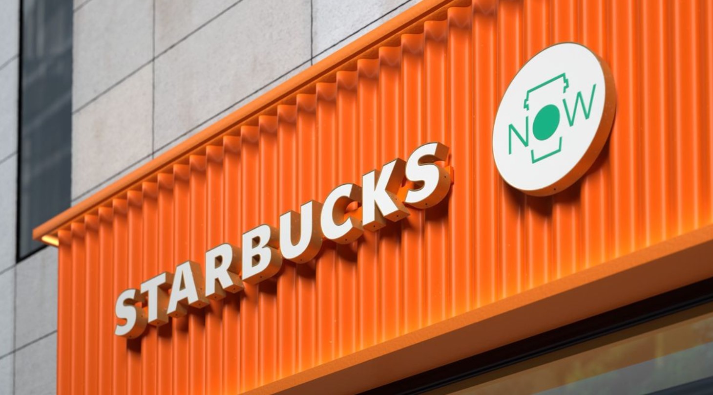 Fachada da Starbucks com letras brancas tridimensionais sobre parede laranja.