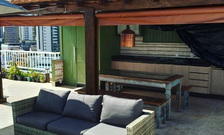 Toldo retrátil sombreando pátio urbano com área gourmet, sofá de vime e vista panorâmica.