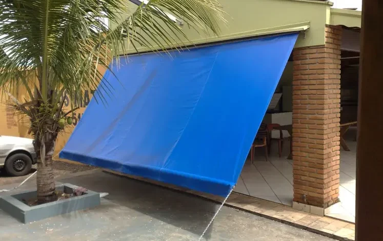 Toldo retrátil azul cobrindo área externa com vaso de palmeira.