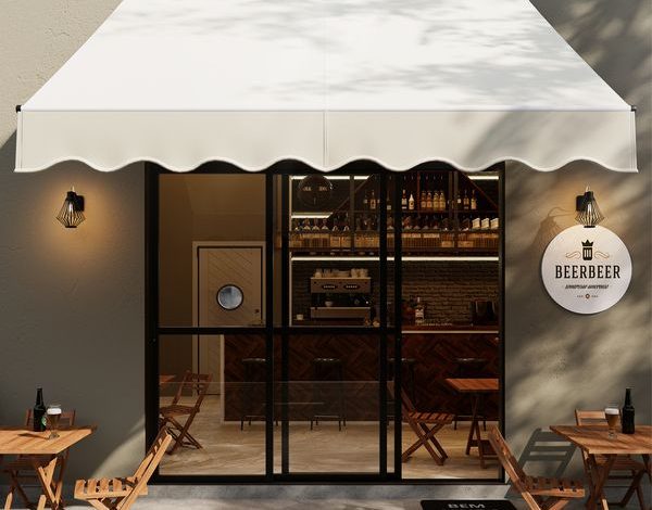 Toldo retrátil creme cobrindo fachada comercial com entrada envidraçada e placa.