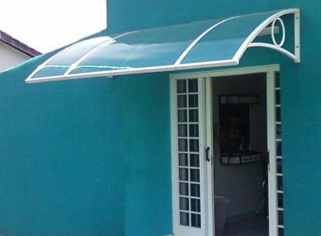 Toldo curvo de policarbonato sobre porta de vidro com estrutura metálica branca.