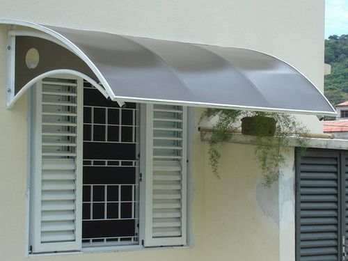 Janela com toldo curvo de Policarbonato cinza, grade preta e planta decorativa.
