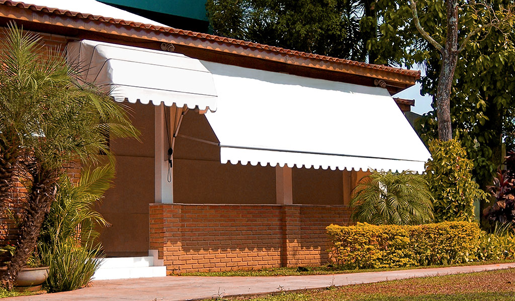 Toldo retrátil branco sombreando varanda de casa com fachada de tijolos