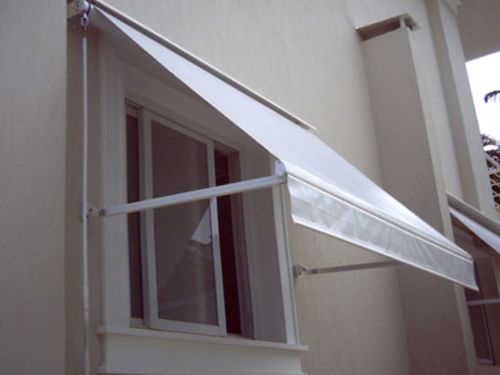 Toldo branco retrátil instalado sobre janela externa de construção residencial.