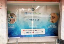Adesivo perfurado exibe serviços médicos e odontológicos em vitrine comercial.