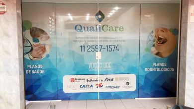 Adesivo perfurado exibe serviços médicos e odontológicos em vitrine comercial.