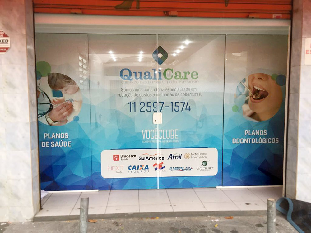 Adesivo perfurado exibe serviços médicos e odontológicos em vitrine comercial.