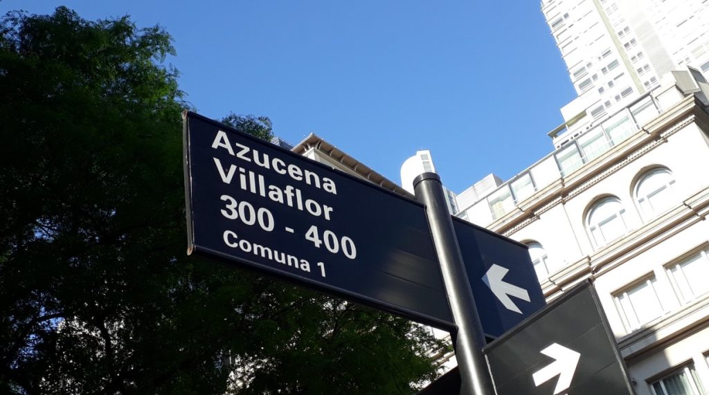 Placa urbana indica Azucena Villaflor, direção e numeração da rua.