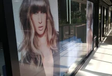 Vitrine com adesivo perfurado exibe modelos e marca de beleza.