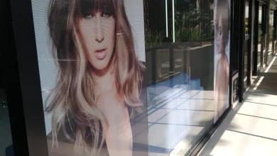 Vitrine com adesivo perfurado exibe modelos e marca de beleza.