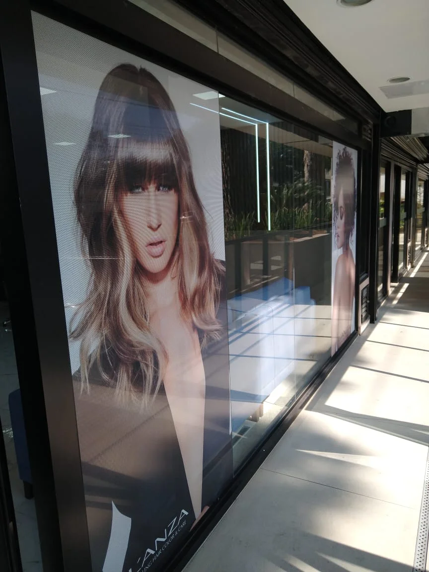 Vitrine com adesivo perfurado exibe modelos e marca de beleza.