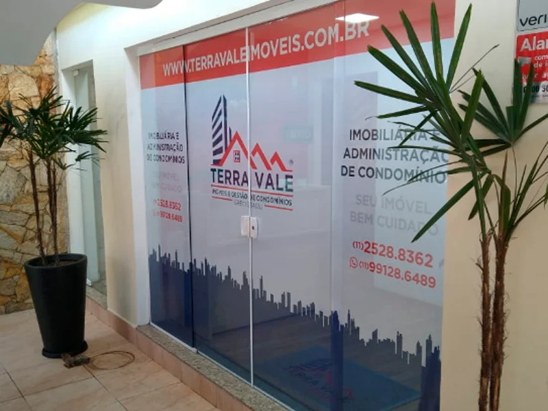 Vitrine imobiliária com adesivo perfurado e informações de contato visíveis.