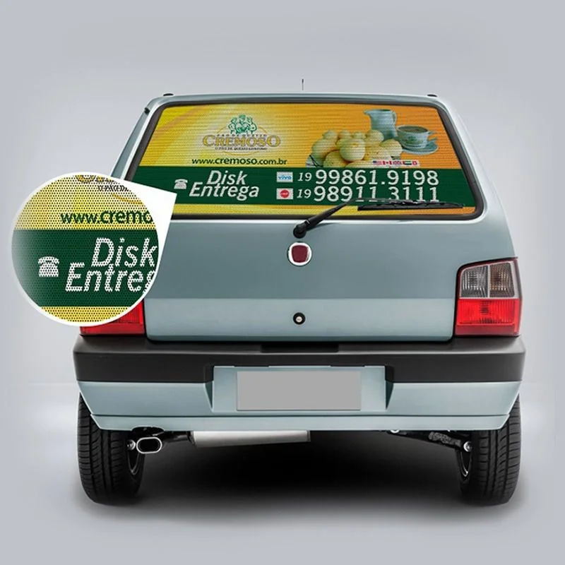Carro com adesivo perfurado exibe marca Cremoso e contatos visíveis.