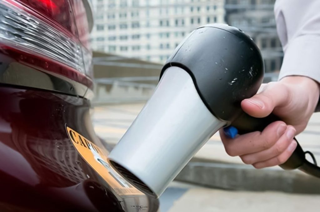 Pessoa usa secador para soltar adesivo em carro urbano.