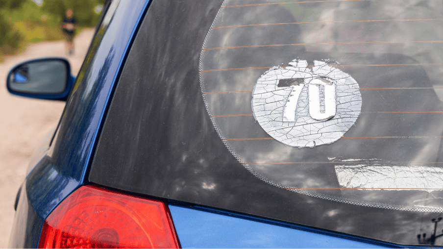 Adesivo antigo e ressecado com número 70 em vidro automotivo.